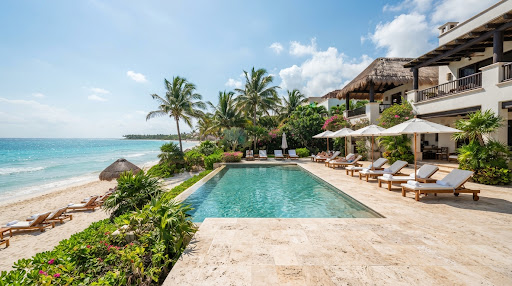 Wide perspective of the private travertine stone pool deck with teak loungers and infinity pool